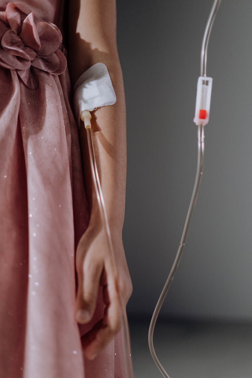 a girl in pink dress with blood transfusion set on her arm
